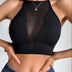 A woman wearing the Women’s Mesh Backless Crop Top—a sleeveless, black, ribbed camisole featuring a sheer mesh center panel—paired with blue jeans and a necklace.